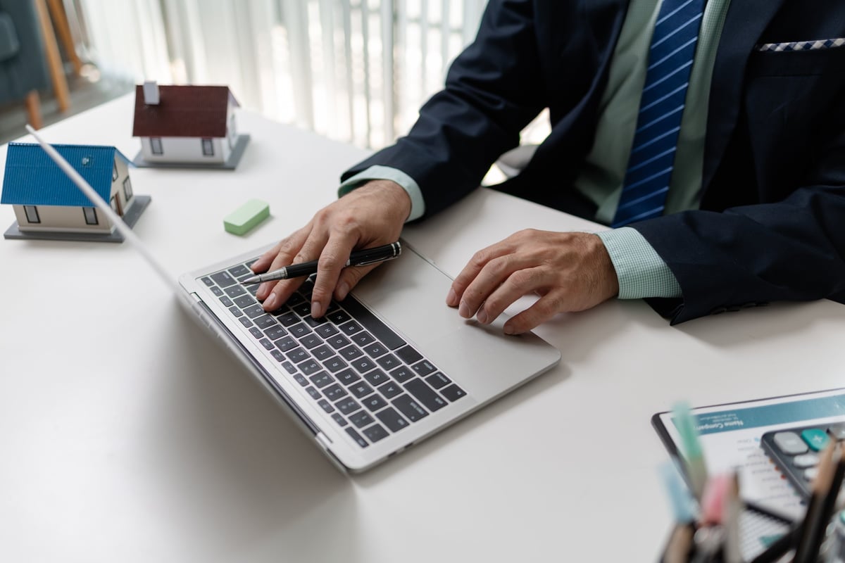 Businessman working on laptop while calculating property investment with house models on desk, representing real estate planning, finance analysis, and decision making in property business.