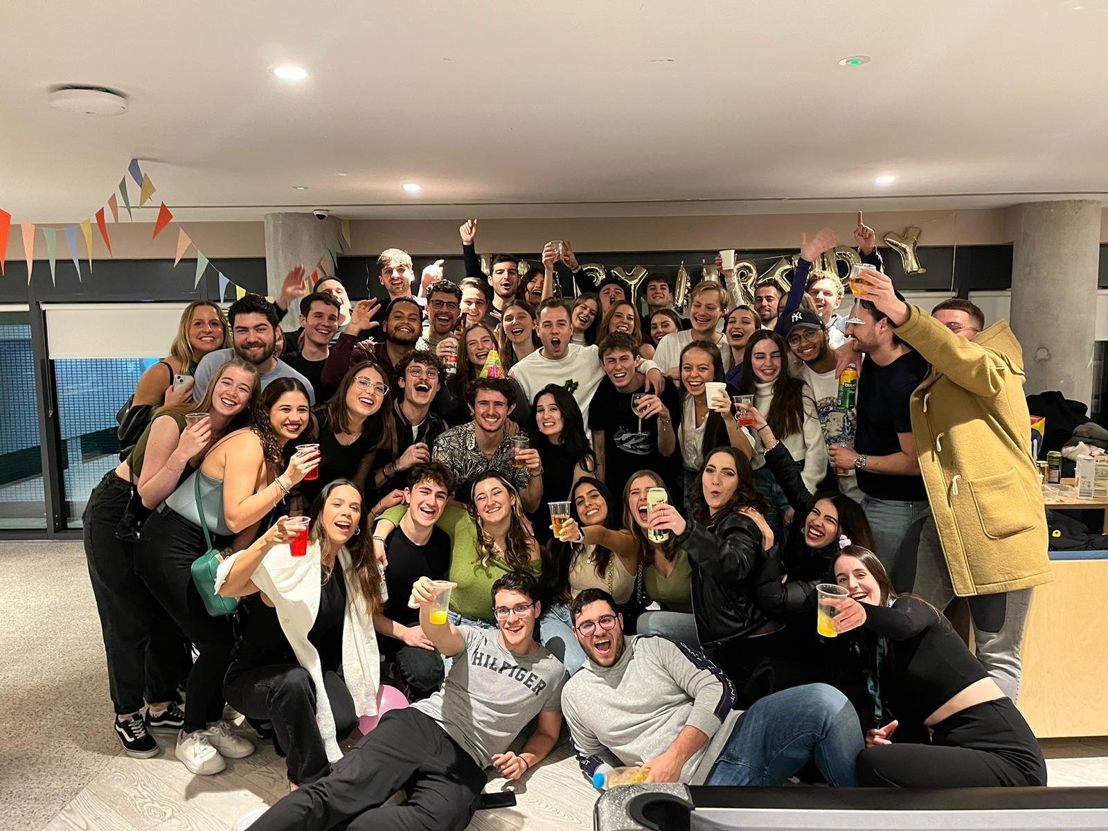 Large diverse group of people posing together indoors for a celebratory team photo, smiling and waving at the camera