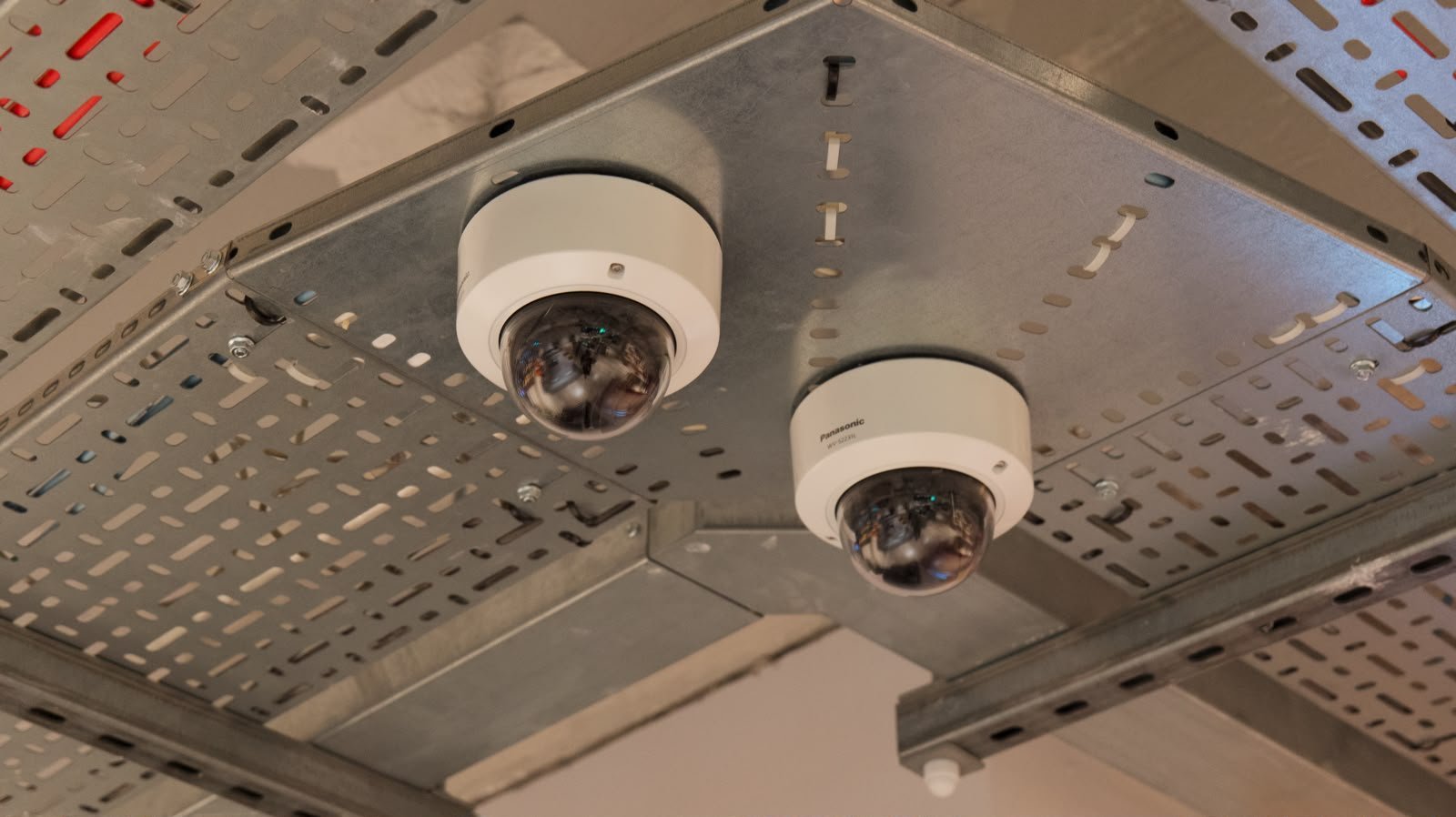 Two white dome security cameras mounted on a ceiling with visible wiring and infrastructure